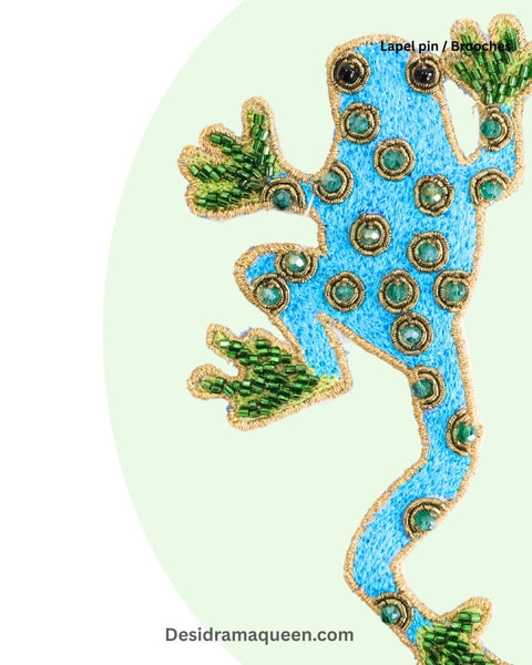 Handmade frog-shaped brooch with blue embroidery and green beaded accents, quirky statement accessory.