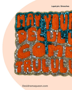 Quirky handmade brooch with embroidered text ‘May Your Delulu Come Trululu’ in orange and teal beads, statement lapel pin accessory.