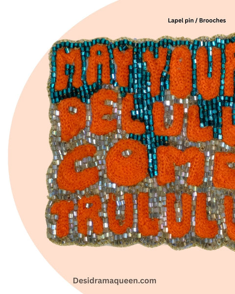 Quirky handmade brooch with embroidered text ‘May Your Delulu Come Trululu’ in orange and teal beads, statement lapel pin accessory.