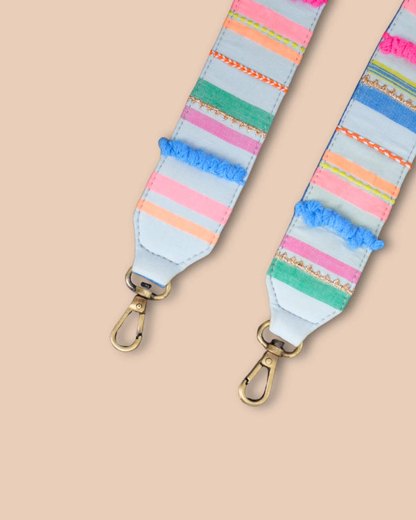 Colorful striped bag strap with gold hardware on a beige background
