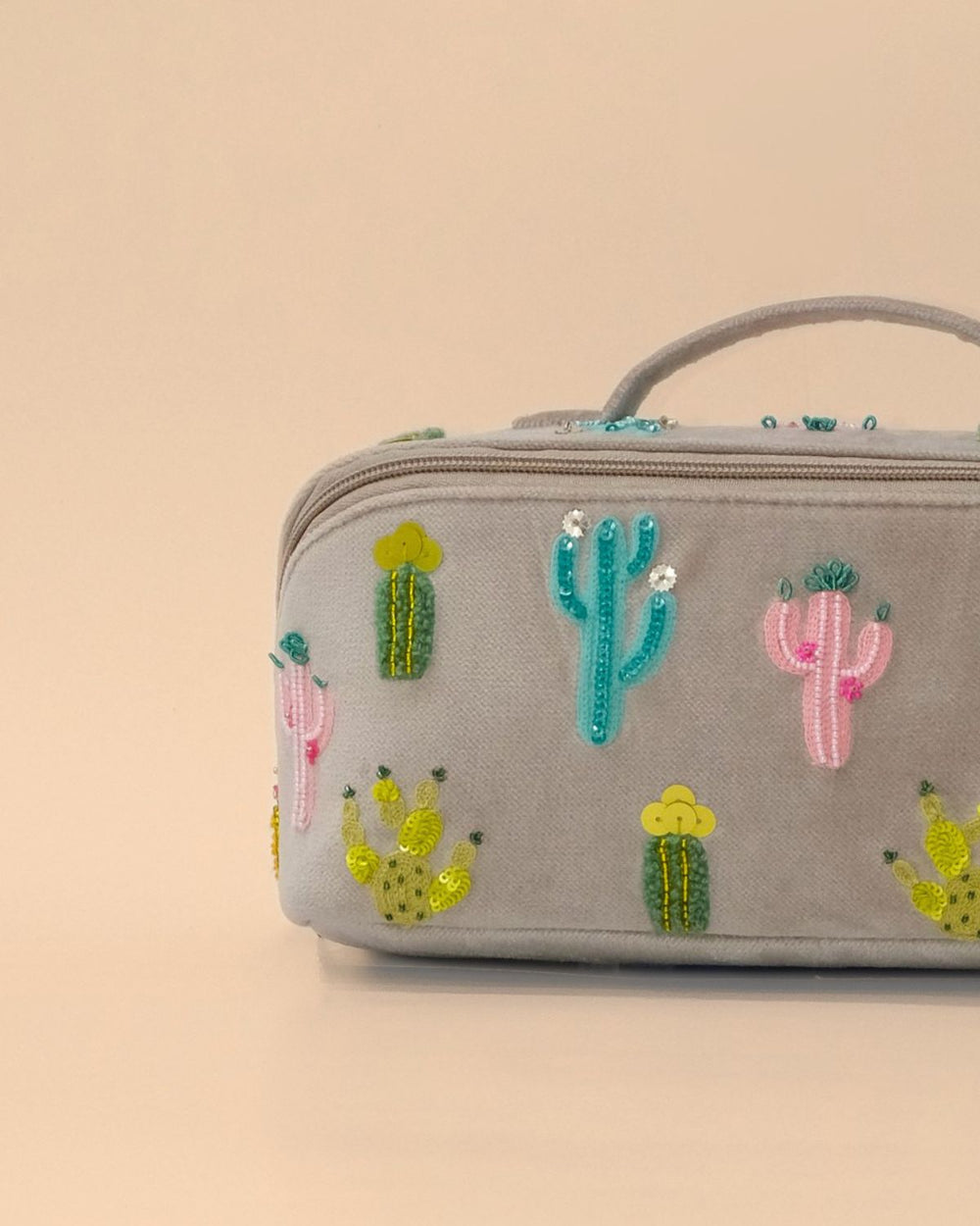 Front view of the Cactus Sand Shell Makeup Pouch featuring colorful embroidered cactus motifs on light grey fabric with a zip closure, top handle, and spacious design for cosmetics and travel essentials.