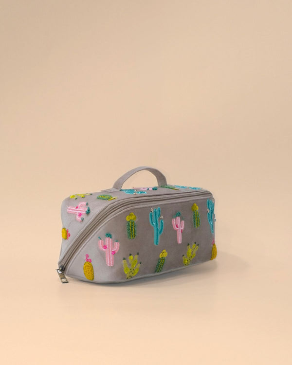 Angled view of the Cactus Sand Shell Makeup Pouch highlighting its embroidered cactus pattern, structured rectangular silhouette, sturdy top handle, and spacious zippered compartment.