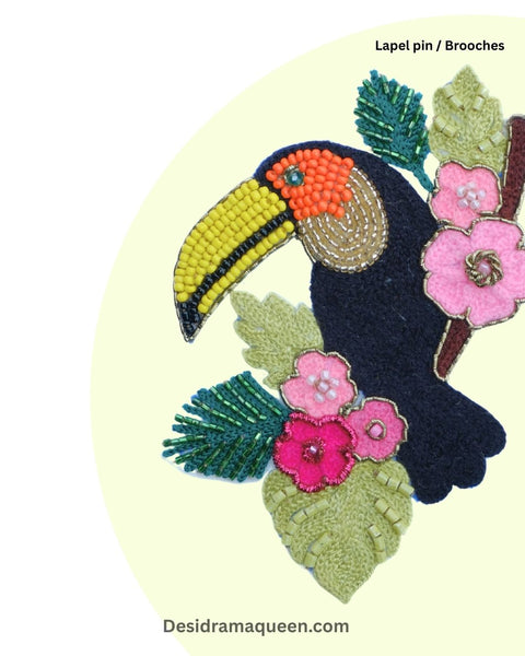 Beaded toucan brooch featuring yellow beak, pink floral embroidery, and green leaf details.