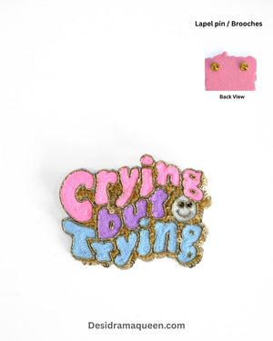 Colorful embroidered brooch with text ‘Crying but Trying’ in pink, purple, and blue with beaded details – handmade quirky statement pin.