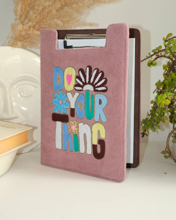 Pink notebook with 'Do Your Thing' text and colorful design on a white surface.