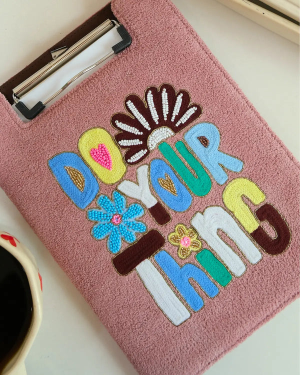 Pink clipboard with colorful text and floral designs on a white surface.