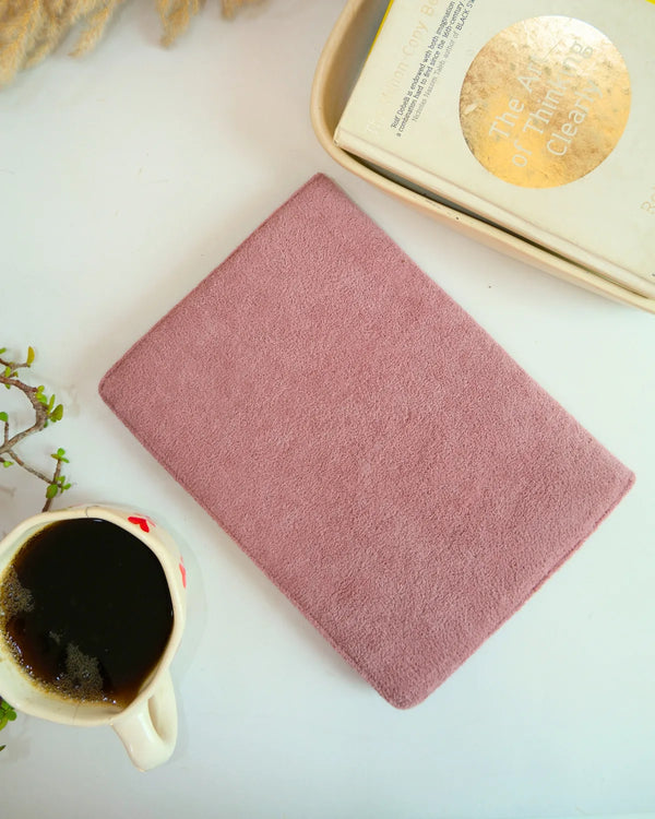 Pink notebook on a white surface with a cup of coffee and a book.