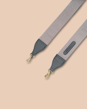 Gray and navy bag strap with gold hardware on a beige background