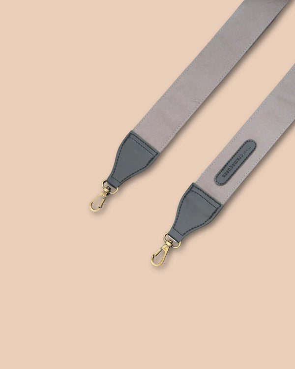 Gray and navy bag strap with gold hardware on a beige background