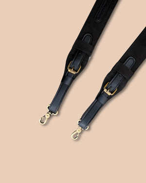 Black leather bag strap with gold hardware on a beige background