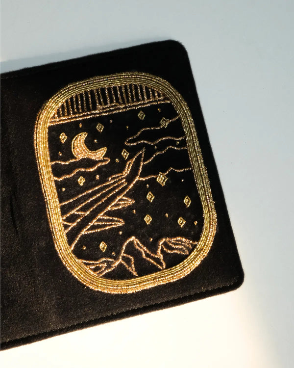 Black fabric patch with gold embroidery of a celestial design on a light gray background