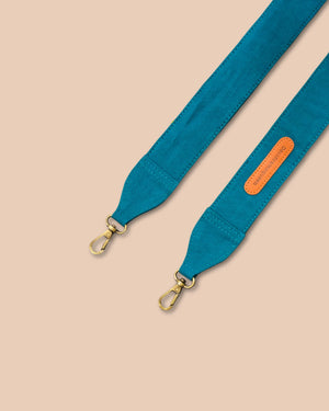 Teal bag strap with gold hardware on a beige background