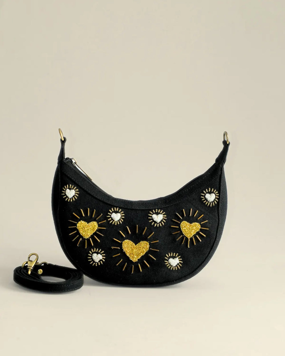 Black crescent-shaped bag with gold heart and star designs on a beige background