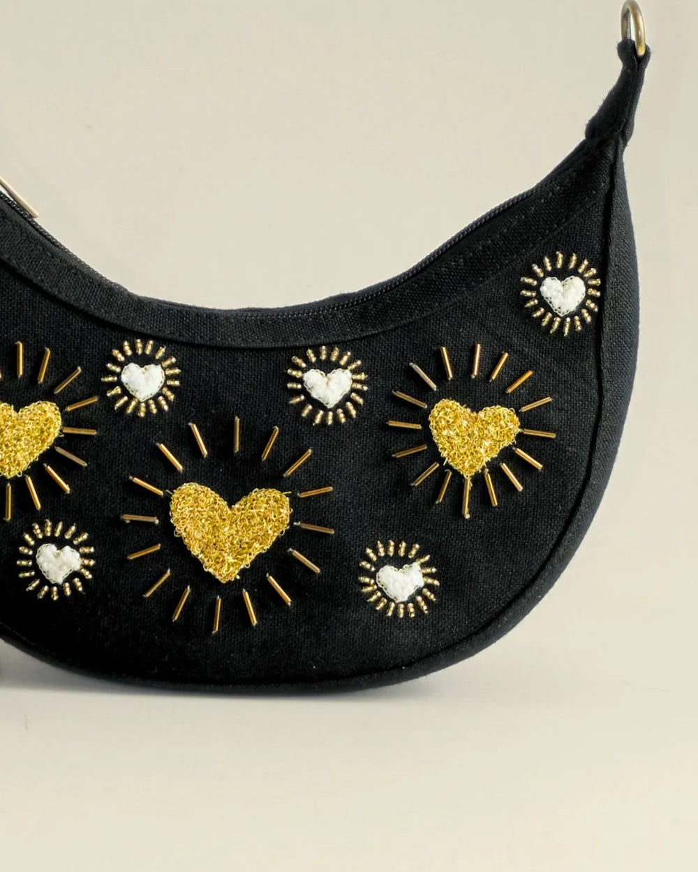 Black crescent-shaped bag with gold heart and star designs on a beige background
