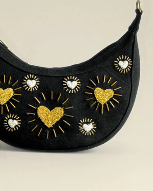 Black crescent-shaped bag with gold and white heart designs on a beige background