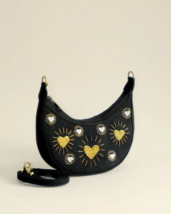 Black handbag with gold heart and sun designs on a beige background