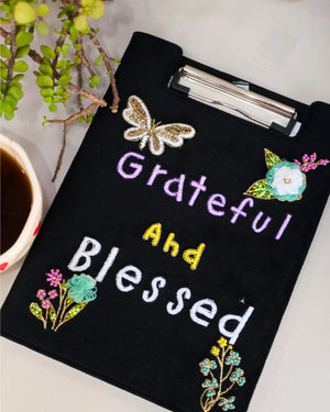 Black clipboard with 'Grateful and Blessed' text and floral designs on a white background