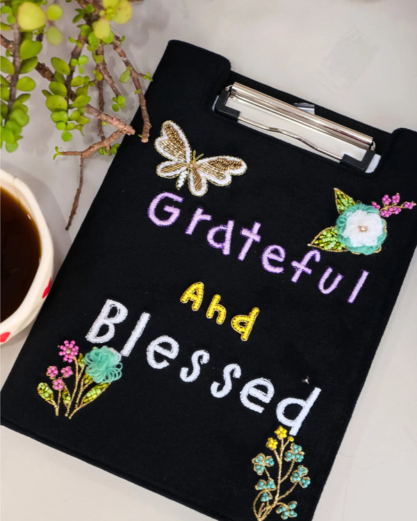 Black clipboard with 'Grateful and Blessed' text and floral designs on a white background