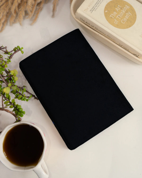 Black notebook on a white surface with a cup of coffee and decorative elements.