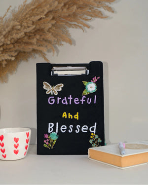 Black clipboard with 'Grateful and Blessed' text, decorative elements, and a white surface with decor items.