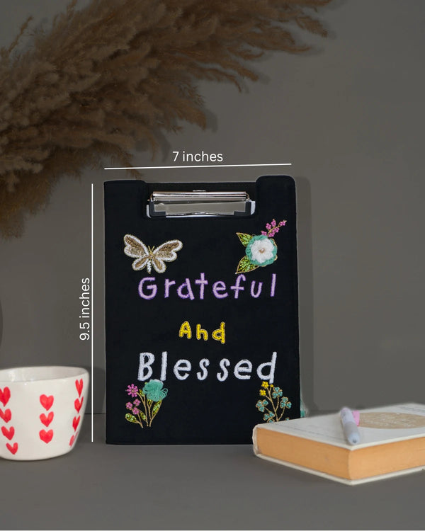 Black clipboard with 'Grateful and Blessed' text and measurements on a gray background