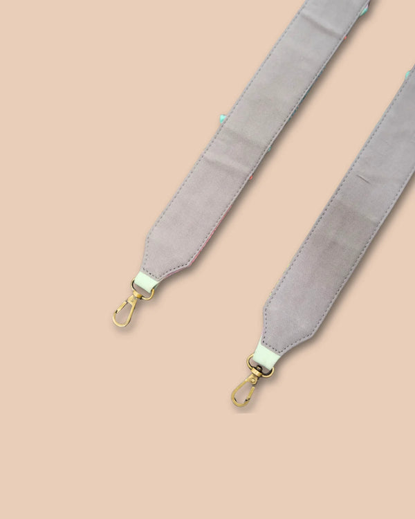 Gray bag strap with gold hardware on a beige background