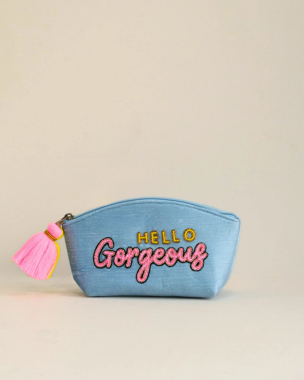 Blue pouch with 'Hello Gorgeous' text and pink tassel on a beige background