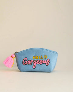 Blue pouch with 'Hello Gorgeous' text and pink tassel on a beige background