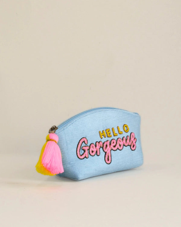 Light blue pouch with 'Hello Gorgeous' text and tassels on a beige background