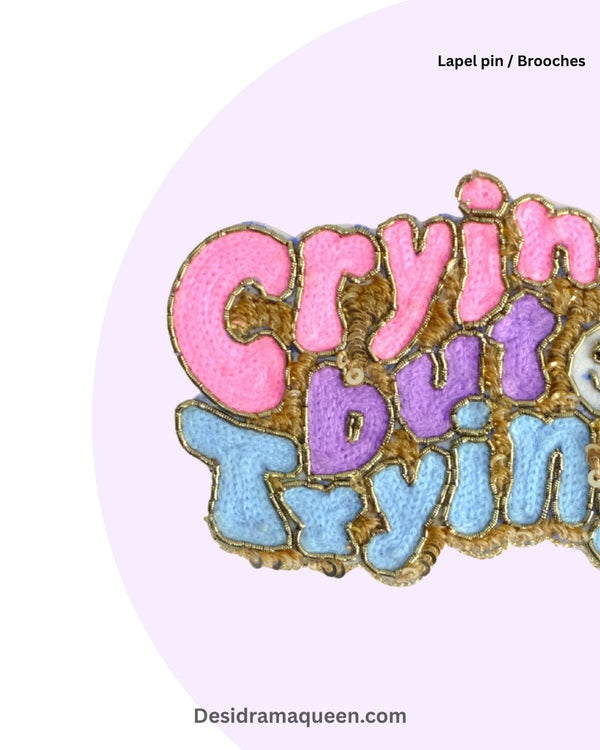 Quirky embroidered brooch with pastel text ‘Crying but Trying’ and beaded outline, handmade statement lapel pin for bags, jackets, and scarves.