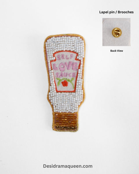 Self Love Sauce brooch in beaded design with white, gold, and pastel pink embroidery, handmade motivational lapel pin for jackets and bags.