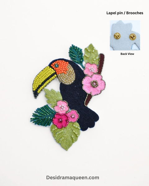 Handmade toucan brooch with beadwork, pink flowers, and green leaves for tropical fashion style.