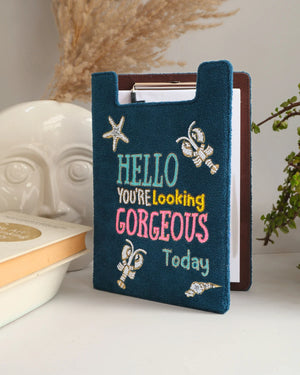 Blue embroidered book cover with 'Hello, you're looking gorgeous today' text on a white surface.