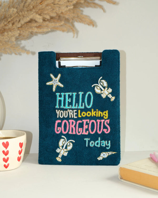 Blue embroidered clipboard with decorative text and embellishments on a neutral background