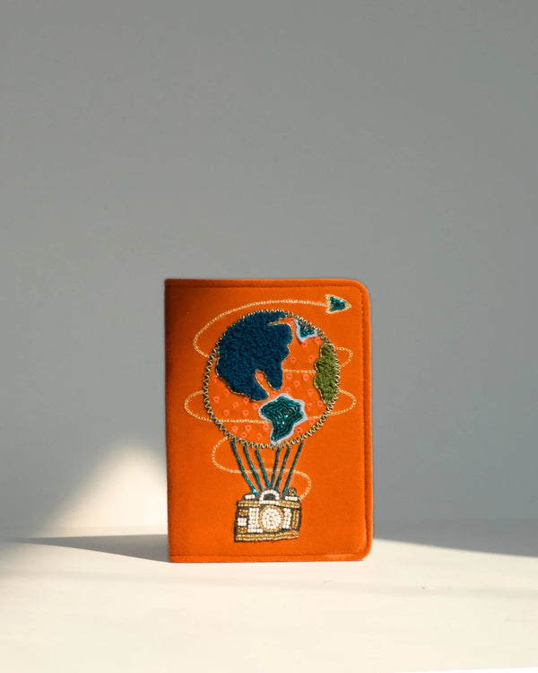 Orange passport holder with hot air balloon design on a gray background