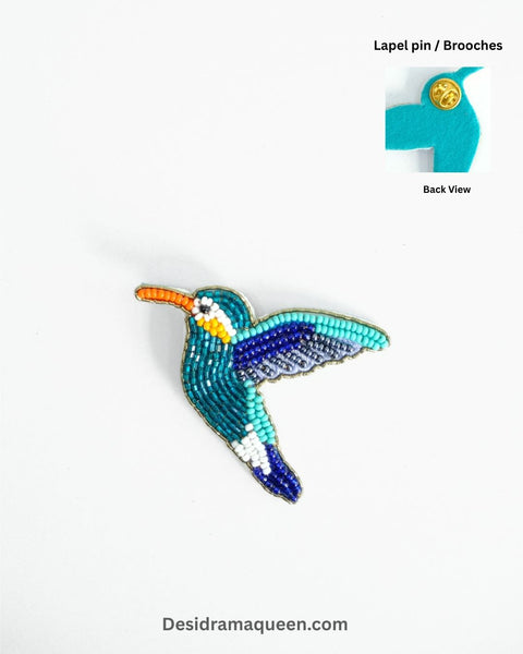 Handmade embroidered brooch in the shape of a kingfisher bird with turquoise, blue, orange, and white beadwork.