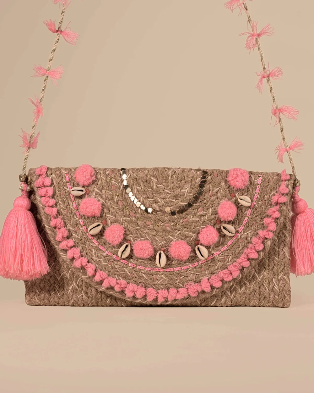 Clutch bag with pink pom-poms and tassels on a beige background