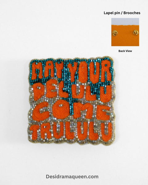 Handmade embroidered brooch with orange text and teal bead accents, quirky ‘May Your Delulu Come Trululu’ lapel pin for jackets and bags.