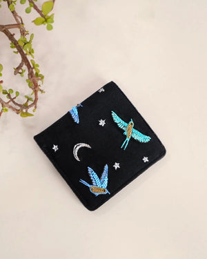 Black pouch with blue bird and star designs on a beige background