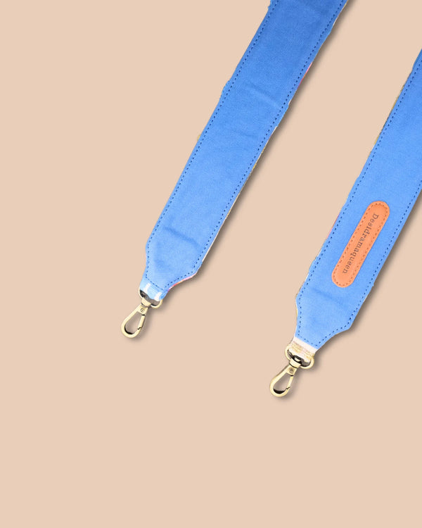 Blue bag strap with gold hardware on a beige background