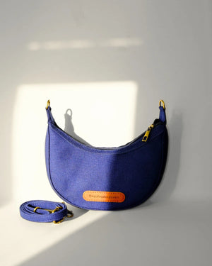 Blue crossbody bag with an orange label on a light gray background