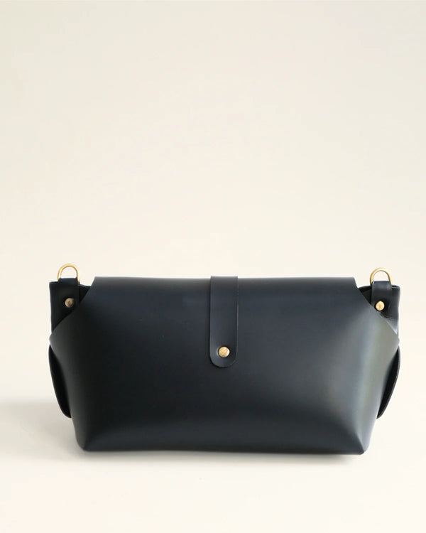 Black leather handbag with gold hardware on a light beige background
