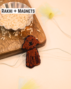 Cute Dog embroidered rakhi magnet placed beside a bowl of rice, styled for a festive Raksha Bandhan celebration.