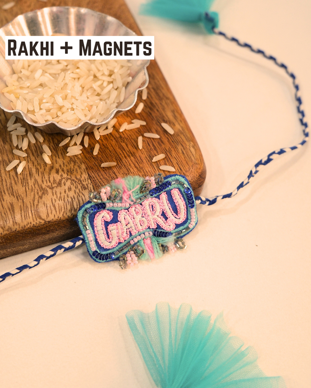 Gabru embroidered rakhi with glitter lettering placed beside a bowl of rice for a festive Raksha Bandhan celebration.