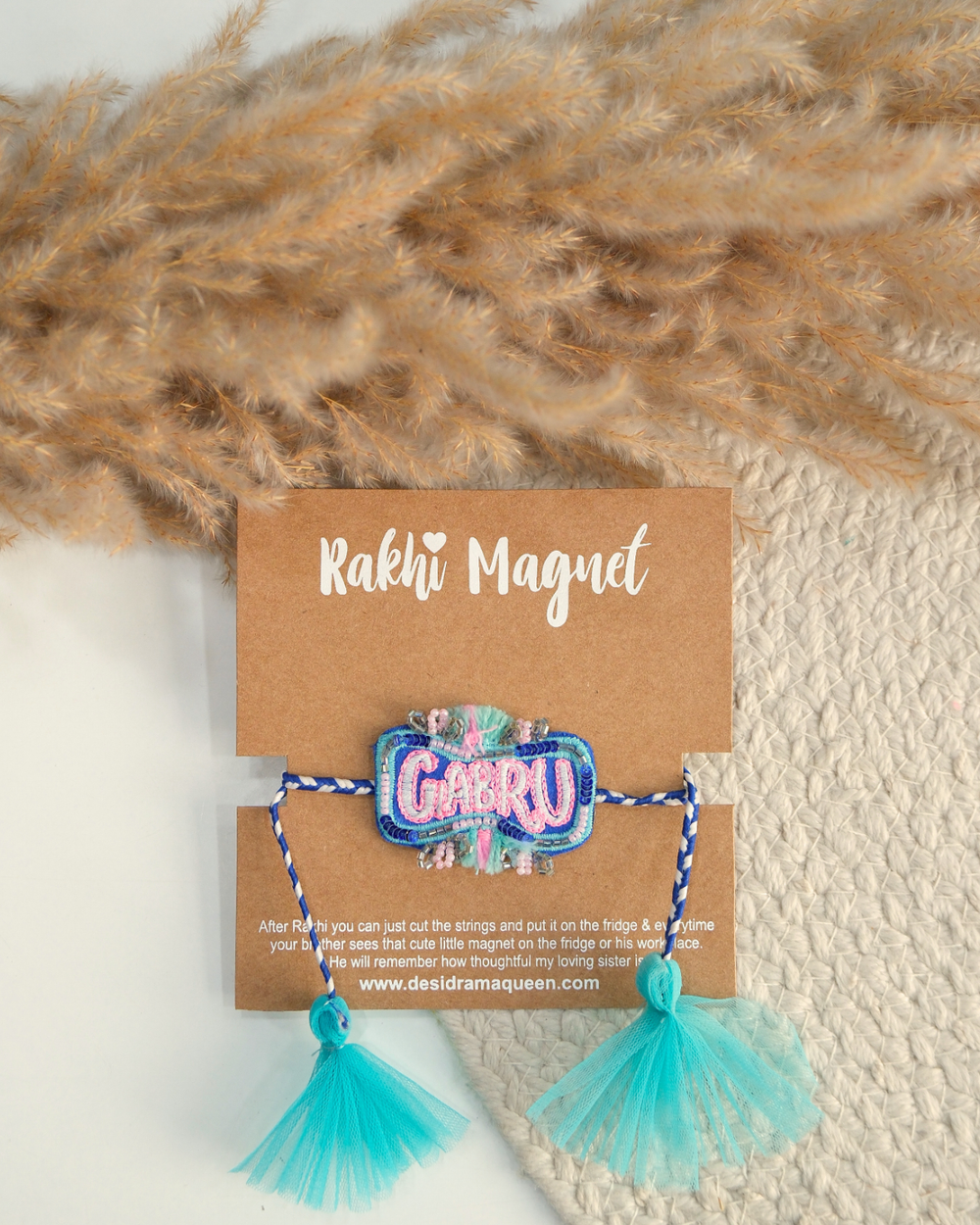 Gabru embroidered rakhi with glitter lettering placed beside a bowl of rice for a festive Raksha Bandhan celebration.