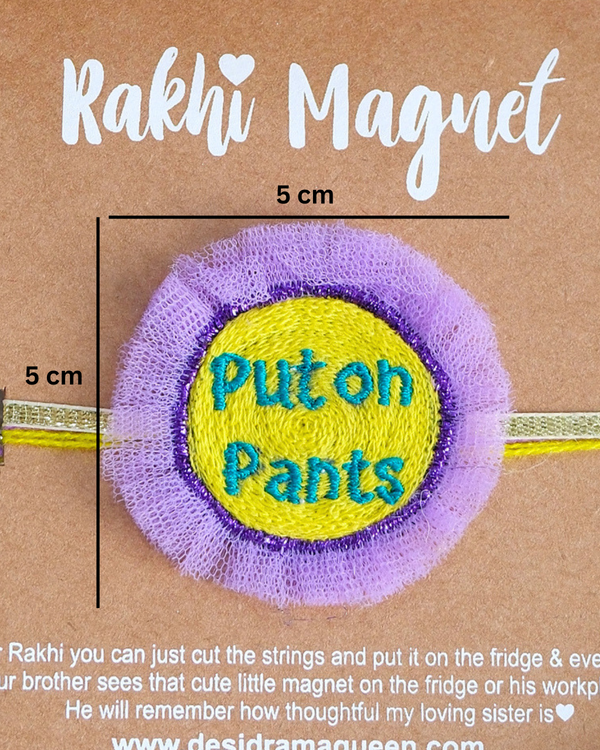 Close-up of Put On Pants embroidered rakhi magnet on display card, showcasing handcrafted design and reusable keepsake fridge magnet.