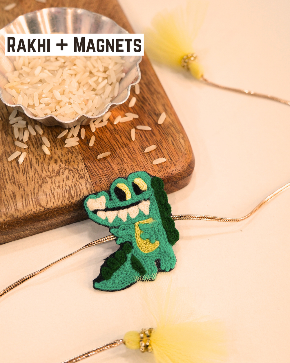 Crocodile embroidered rakhi magnet placed beside a bowl of rice, styled for a festive Raksha Bandhan celebration.