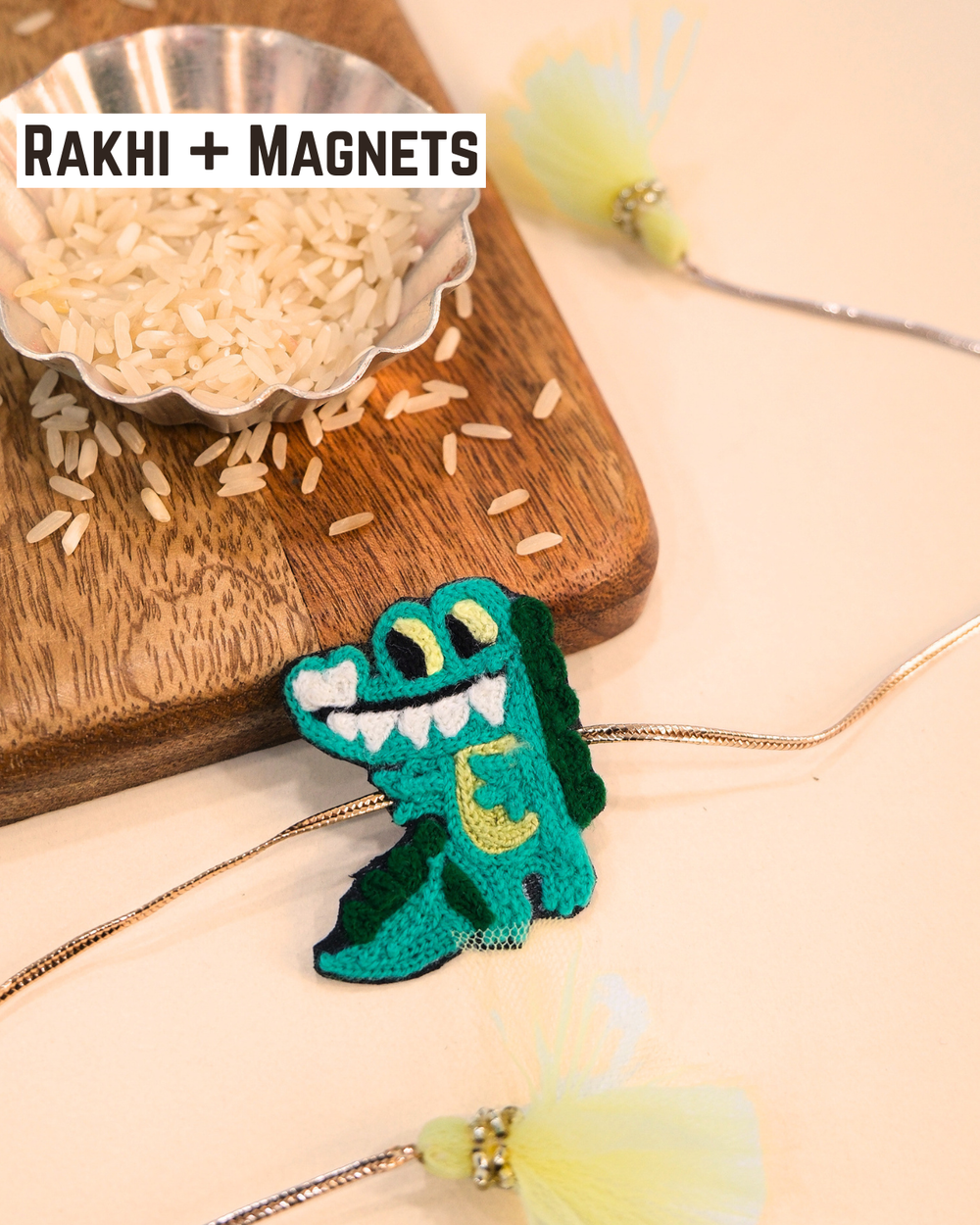 Crocodile embroidered rakhi magnet placed beside a bowl of rice, styled for a festive Raksha Bandhan celebration.