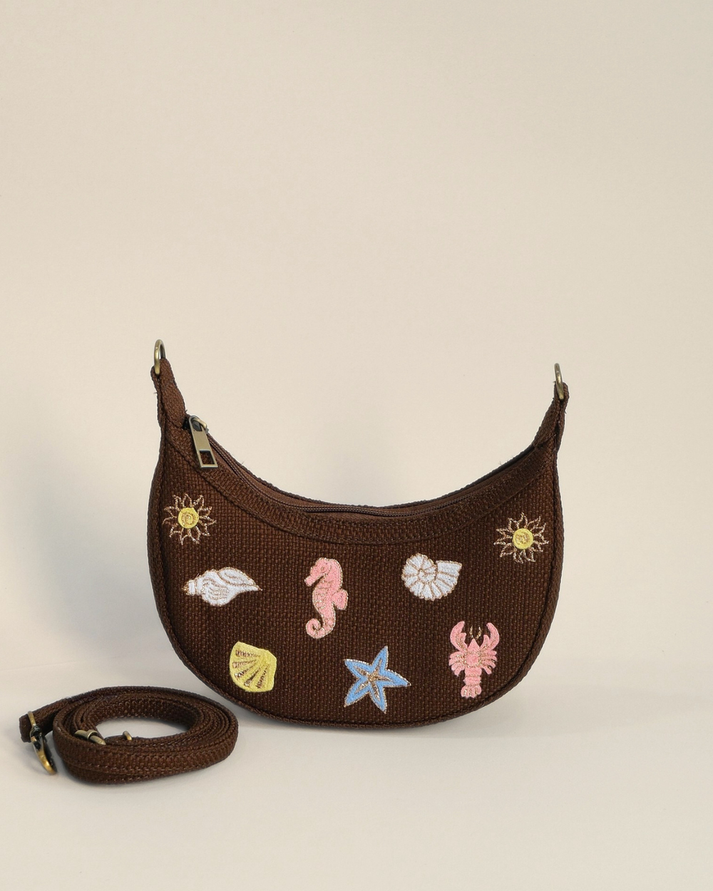 Brown Sea Spark Mini Banana Bag featuring colorful embroidered seashell, seahorse, lobster, starfish, and sun motifs on textured woven fabric with a detachable shoulder strap.