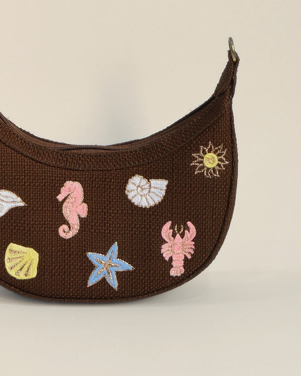 Brown Sea Spark Mini Banana Bag featuring colorful embroidered seashell, seahorse, lobster, starfish, and sun motifs on textured woven fabric with a detachable shoulder strap.
